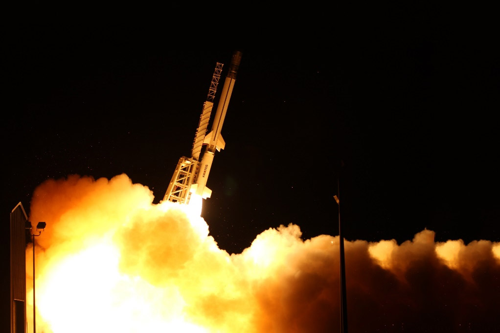 Kratos Zeus solid rocket motor launching into the night sky with bright flames and smoke illuminating the dark surroundings.
